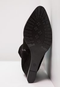 Zwarte suède laars met een spitse neus en een gestructureerd rubberen zool. Voorzien van een lage hak en een zijrits. De zool heeft een patroon voor extra grip.