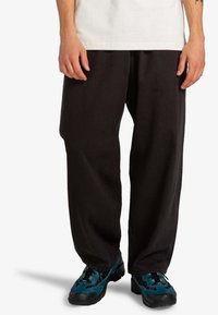 Black wide-leg pants made from durable fabric, featuring a loose fit, paired with blue and black athletic shoes.