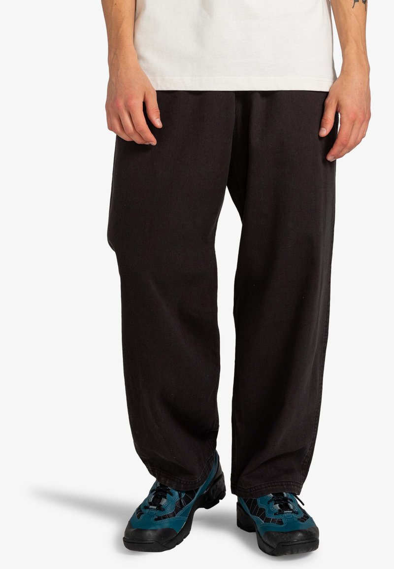 Black wide-leg pants made from durable fabric, featuring a loose fit, paired with blue and black athletic shoes.