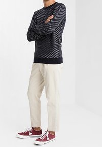 Marineblauwe trui met witte stippen, crèmekleurige textuurbroek en bordeauxrode sneakers. Geribbelde boorden en tailleband van de trui. Casual pasvorm.