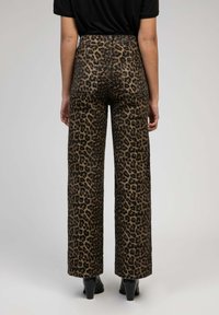 Des pantalons larges en imprimé léopard présentent une taille haute, un matériau en denim, des poches arrière et une texture lisse, associés à des bottes à talons noires.