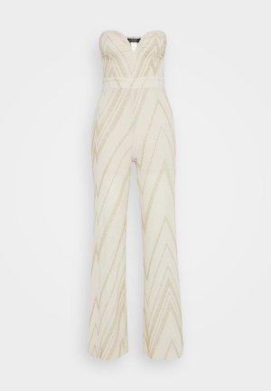 Trägerloser Jumpsuit in Creme mit goldenem Zickzackmuster, weiten Beinen, tailliertem Schnitt und strukturiertem Stoff. Keine sichtbaren Beschläge oder Verzierungen.