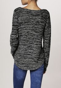 Gestreifter Pullover in Schwarz und Weiß mit langen Ärmeln, strukturiertem Strickstoff, tiefem Rückenausschnitt und abgerundetem Saum, kombiniert mit blauen Jeans.