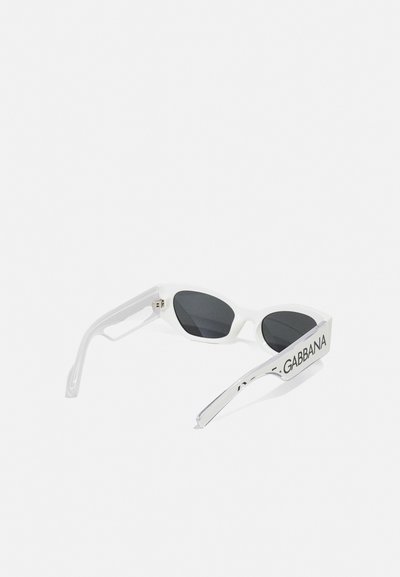 Lunettes de soleil blanches en forme d'œil de chat, avec des verres sombres et des branches marquées du texte "GABBANA". Texture en plastique lisse.