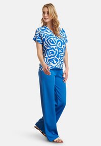 Blue patterned short-sleeve blouse with white abstract designs, paired with solid blue trousers, both made from lightweight fabric.