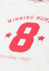 Valge T-särk, millel on suur punane sädelev number 8, üle selle on tekst "VÕITJATE NUMBER" ja allpool roosa tekst "Barcelona 1982".