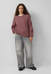 Bordeauxroter, strukturierten Strickpullover mit lockerer Passform, kombiniert mit weit geschnittenen, verblassten grauen Jeans und klobigen schwarzen Schuhen.