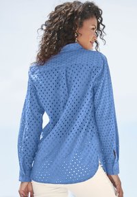Camicetta blu a maniche lunghe con motivi ad occhiello circolare, polsini abbottonati e orlo curvo. Realizzata in tessuto leggero.