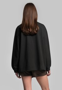 Černá oversized mikina s dlouhými rukávy, vyrobená z bavlny, volný střih, kulatý výstřih a bez viditelných zapínacích detailů.