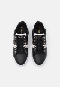 Baskets en simili cuir noir avec une rayure blanche ornée d'un motif floral, des œillets dorés et une semelle en caoutchouc blanche.