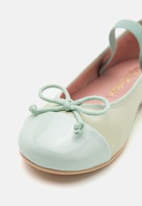 Bailarina en verde menta y beige claro. Punta de charol brillante con un acento de lazo. Cuerpo de tela suave y plantilla de color rosa claro.