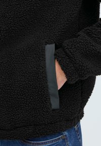Svart fleece-pullover med en strukturert, plysj overflate. Har sidelommer med en glatt, svart kant. Casual design med løs passform.