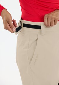 Beige Outdoor-Hosen verfügen über einen Klettverschluss an der Taille. An der Seite zeigt sich ein dezentes Branding-Detail, "W-PRO 10000," in einem hellen Ton.