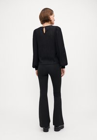 Black ribbed long-sleeve top featuring a back keyhole detail, paired with black flared pants and chunky platform boots.