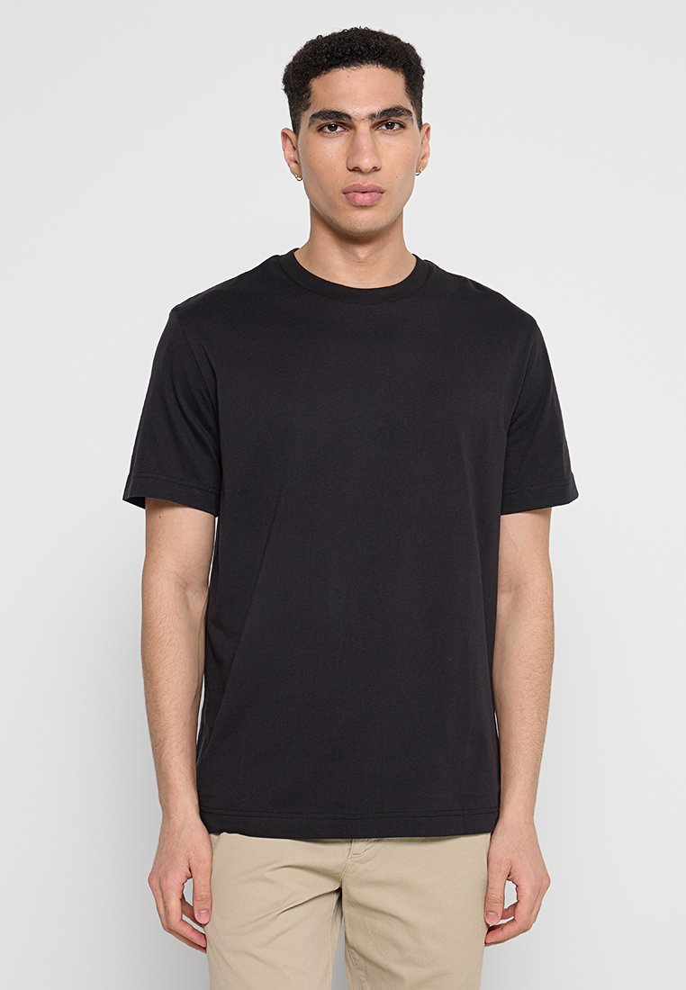 Czarna bawełniana koszulka z krótkim rękawem i okrągłym dekoltem, o gładkiej fakturze i luźnym kroju. Brak widocznych logo lub wzorów.