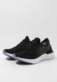 Zapatillas deportivas negras con parte superior de tejido, con un patrón degradado, cordones negros y una suela blanca y texturizada. Logo de Nike en el lateral.