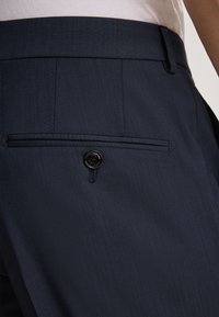 Granatowe, dopasowane spodnie o gładkiej fakturze, z jedną tylną kieszenią zapinaną na czarny guzik oraz subtelnymi pionowymi paskami w tkaninie.