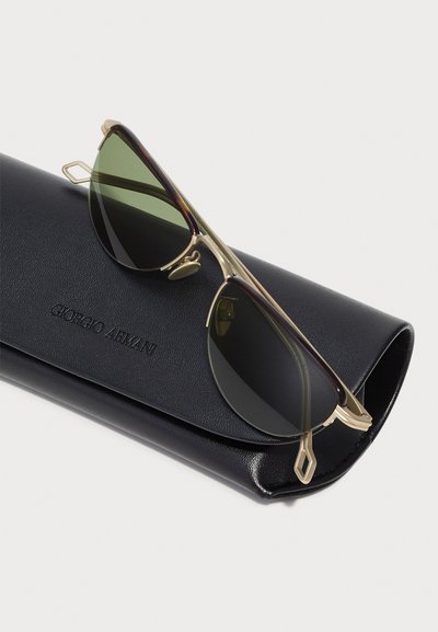 Giorgio Armani sunglasses with green lenses, gold metal frame, and tortoiseshell accents, resting on a black leather case.