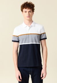 Pikétröja i vit, grå, marinblå och brun randig. Korta ärmar, enfärgad nederdel, krage, tillverkad av andningsbart material.