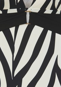 Musta-valkoinen seepra-raidallinen kangas, jossa on kultasävyinen metallikiinnitys vyötäröllä, ja joka on sileä, hieman tekstuuri-ilmeinen.