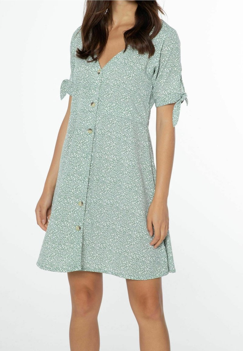 Robe vert menthe avec motif floral blanc, manches courtes avec liens, décolleté en V et boutons sur le devant. Forme A-line et tissu léger.