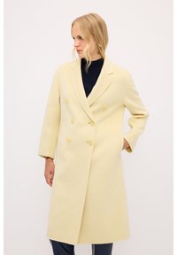 Abrigo de lana amarillo de doble botonadura con solapas grandes, corte recto y dos bolsillos frontales. Tejido texturizado con botones amarillos.