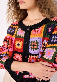 Bunt gestrickte Strickjacke mit einem Patchwork-Design in lebhaften Quadraten aus Rot, Pink, Lila und Grün, mit schwarzem Saum und Knopfverschluss.