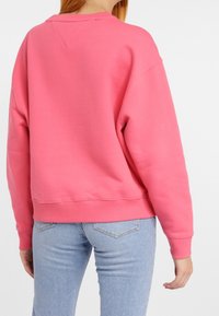 Sweatshirt rose avec une coupe décontractée, des poignets et un col côtelés. Tissu doux avec une texture lisse, associé à un jean bleu clair.