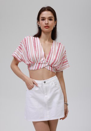 Top court blanc avec des rayures verticales rouges et des motifs géométriques. Associé à une mini-jupe en denim blanc avec une fermeture à boutons à l'avant.