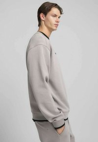 Felpa grigia chiara con dettagli neri, scollo rotondo e polsini a costine. Tessuto morbido, vestibilità rilassata, con un piccolo dettaglio logo sul davanti.