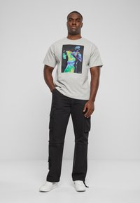 Camiseta de algodón gris con un diseño gráfico colorido centrado en la parte delantera. Combinada con pantalones cargo negros y zapatillas blancas.