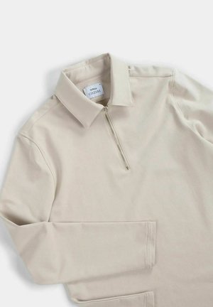 Beige pullover with a zip collar, featuring long sleeves and smooth texture. The material appears soft with a minimalistic design.