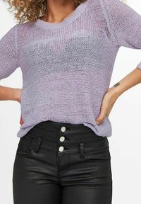 Vaaleanliila neulepaita, jossa on löysä istuvuus ja leveä pääntie, yhdistettynä korkeavyötäröisiin mustiin farkkuihin, joissa on nappikoristeet.