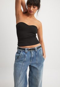 Črn top brez naramnic s prilegajočim krojem, kombiniran z ohlapnimi svetlo modrimi kavbojkami z visokim pasom in izrazitimi šivi.