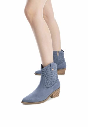 Botas de tobillo azules de ante con detalles de corte láser, puntera afilada y tacón bajo apilado. Presentan una cremallera lateral y un botón decorativo.
