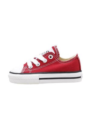 Zapatilla de lona roja con puntera y suela de goma blanca, una franja negra y cordones blancos. Presenta un detalle de costura en la parte superior.