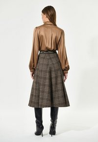 Brun satinbluse med pufærmer, parret med en brun ternet midiskirt. Sorte knæhøje støvler fuldender outfittet. Bæltet har trykt tekst.