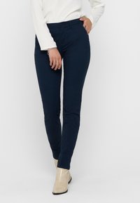 Pantalons ajustés bleu marine en denim, dotés d'un design classique à cinq poches et d'une fermeture à bouton. Texture lisse avec une coupe contemporaine.