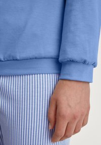 Helles blaues Baumwoll-Sweatshirt mit geschmoktem Bund, kombiniert mit blauen und weißen gestreiften Hosen, die einen glatten Stoff und eine enge Passform zeigen.