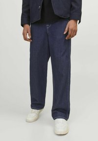 Temno modri jeans hlače s sproščenim krojem, belim šivom in ravnim krojem, v kombinaciji z belimi supergami.