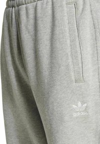 Šedé bavlnené tepláky s jemnou textúrou, elastickým pásom, bočnými vreckami a bielym logom adidas na dolnej časti nohy.