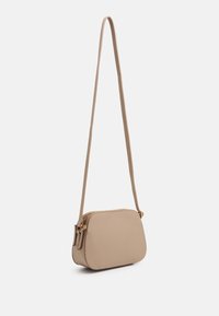 Beige crossbody-taske med lynlås, glat tekstur, rund form og en lang justerbar rem, fremhævet med guldfarvet beslag.