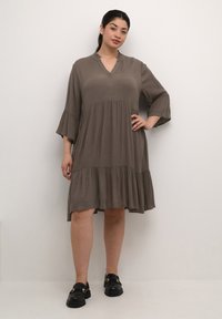 Robe marron, longueur genoux, en tissu léger, avec un décolleté en V, un col à volants et des manches évasées. Jupe à deux niveaux avec une finition texturée.