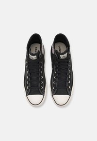 Zapatillas altas de lona negras con puntera de goma blanca y detalles de costura. Presentan cordones negros y la clásica marca All-Star en los laterales.