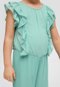 Lichtblauwe jumpsuit met gerimpelde mouwen, geplooide stof rond de taille en benen, zachte textuur en een ronde halslijn.
