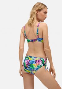 Bikini multicolor con un patrón de hojas tropicales, que cuenta con tirantes ajustables y un detalle de lazo en la parte inferior de cintura baja.