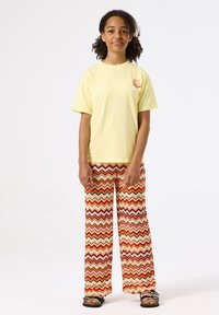 T-shirt en coton jaune avec un petit graphique sur la poitrine, associé à un pantalon large à motifs zigzag multicolores. Sandales noires.