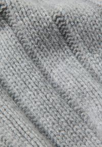 Szara dzianina z teksturowanym wzorem, zawierająca różne rozmiary ściegów. Materiał wydaje się miękki i lekko puszysty.