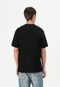 T-shirt in cotone nero con maniche corte e vestibilità rilassata, caratterizzato da un collo rotondo. Indossato con jeans in denim blu chiaro.