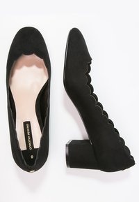 Black suede block-heeled shoes with scalloped edges and an almond toe. The interior is light-colored with a branded insole.
